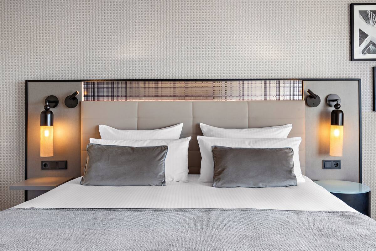 Une chambre d’hôtel moderne avec un grand lit, deux tables de chevet et des lampes fixées au mur.