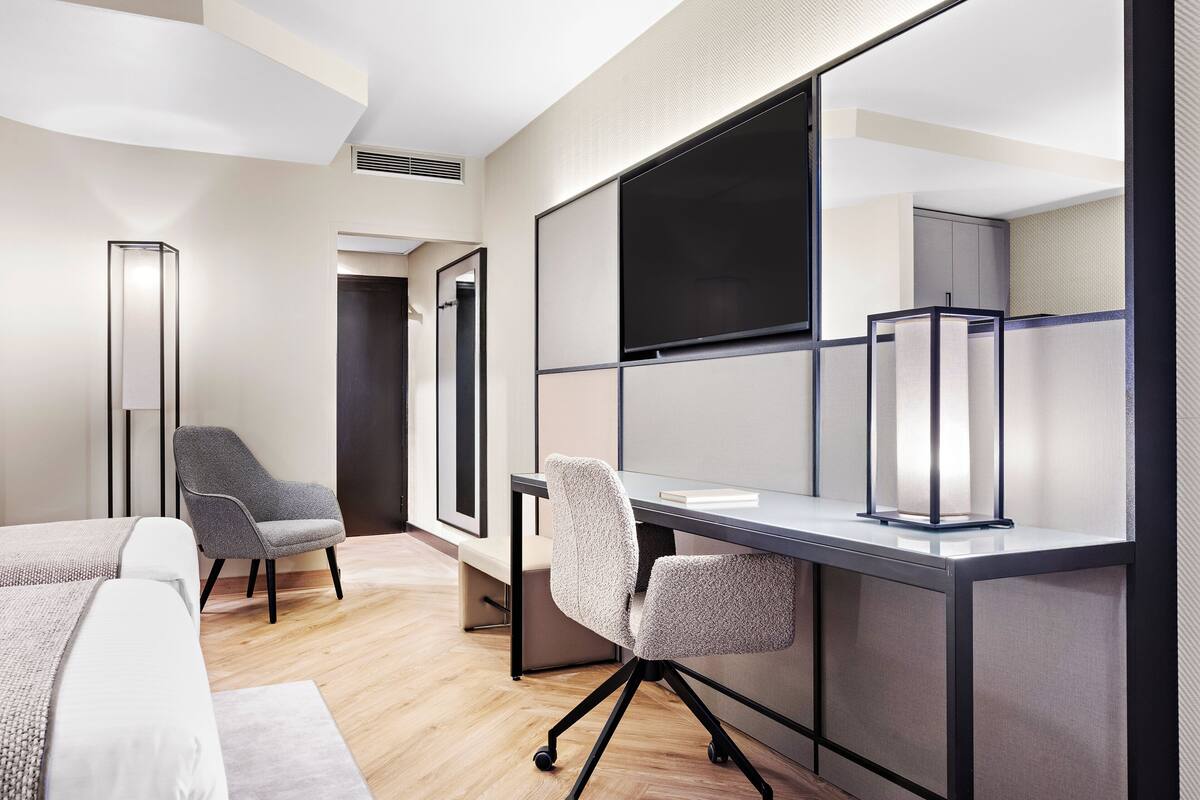Een moderne hotelkamer met een groot bureau, twee stoelen, een bed en een groot raam.