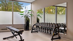 Une salle de sport équipée de matériel d’exercice, dotée de grandes fenêtres et agrémentée de plantes en pot.