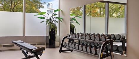 Un gimnasio con equipo de ejercicio, ventanas amplias y plantas en macetas.