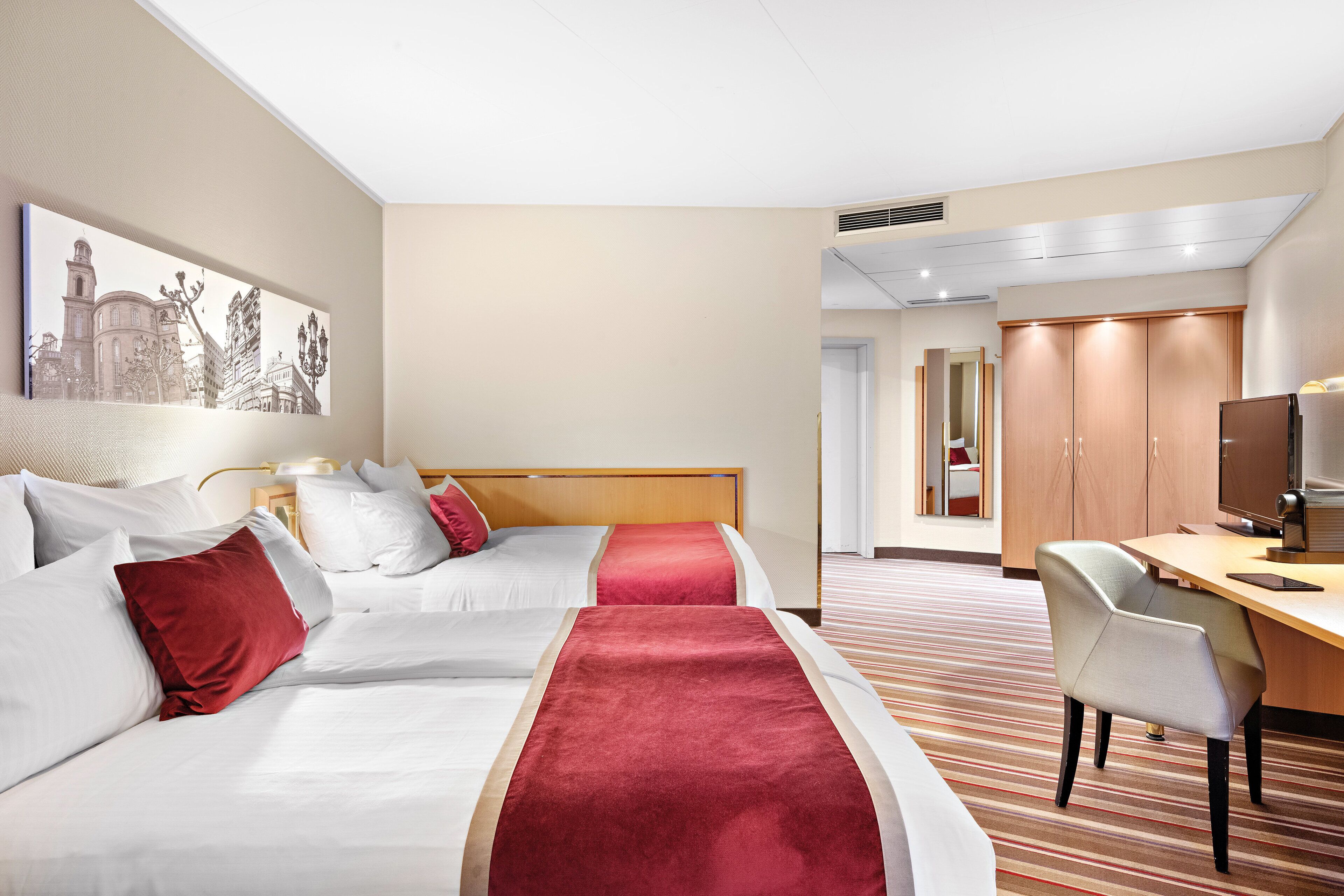 Habitación de hotel con dos camas, un escritorio, una silla y un televisor.