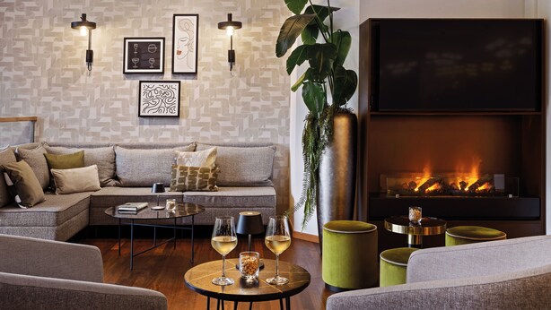 Un salon moderne avec un canapé d’angle, une cheminée et une table basse sur laquelle sont posés des verres de vin.