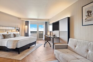 Une chambre d’hôtel avec un lit, un bureau, un canapé et une grande fenêtre donnant sur un beau paysage.