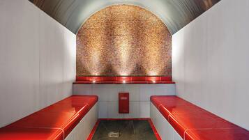 Une salle de bain moderne avec un mur décoré d’une mosaïque, des bancs rouges et une poubelle visible.