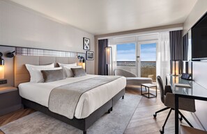 Une chambre d’hôtel moderne dotée d’un grand lit, d’un bureau, d’une chaise et d’un balcon offrant une vue sur la ville.