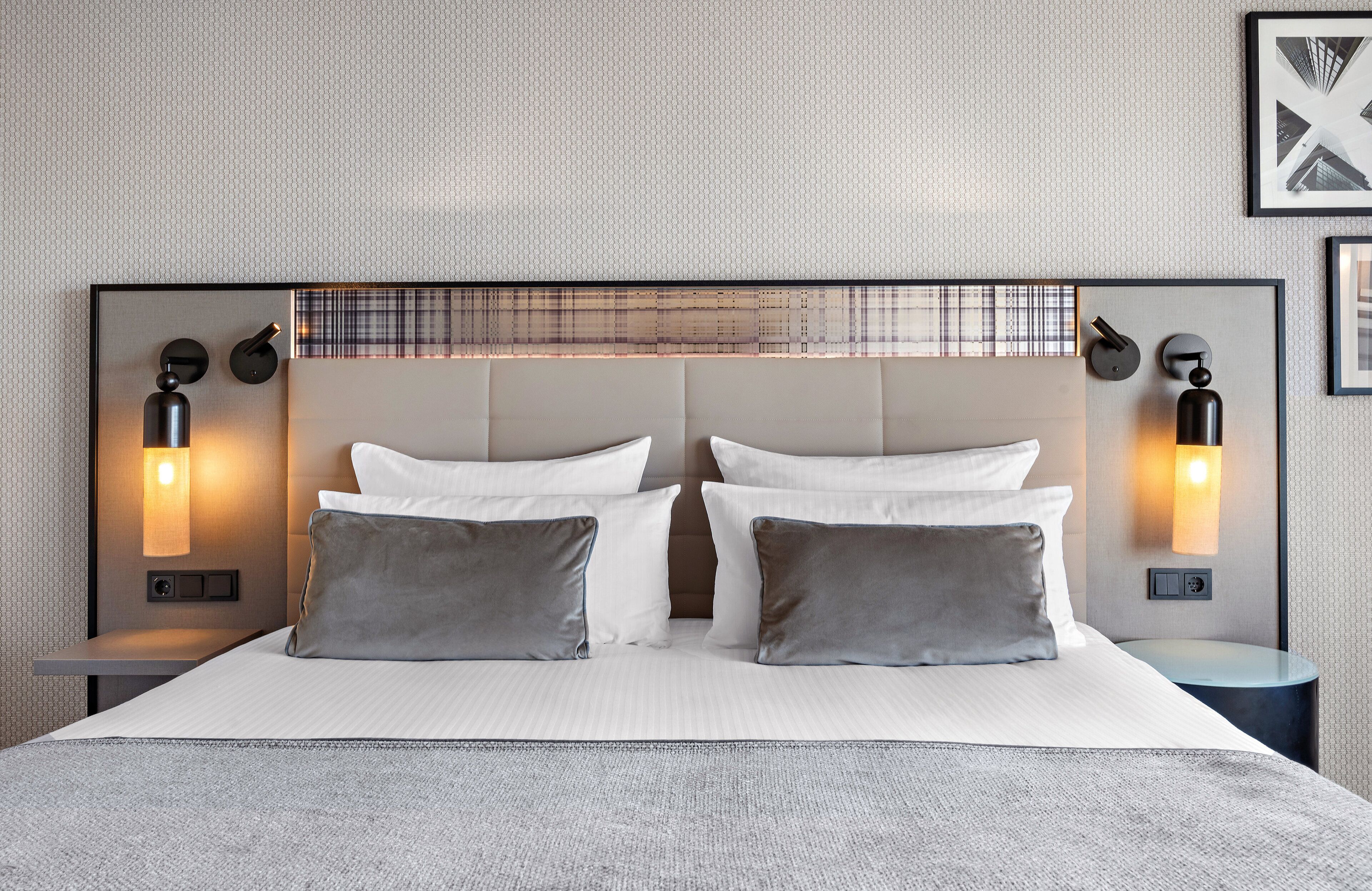 Une chambre d’hôtel moderne avec un grand lit, deux tables de chevet et des lampes fixées au mur.