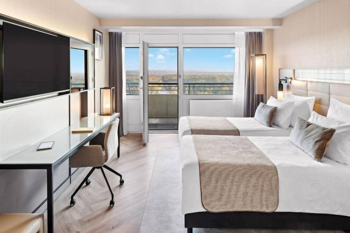 Een hotelkamer met een bed, een bureau, een televisie en een balkon met uitzicht.
