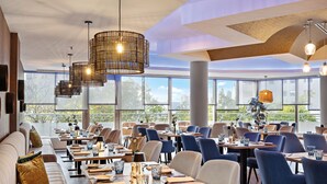 Un restaurant moderne doté de hauts plafonds, de grandes fenêtres et de différents types de mobilier, notamment des tables et des chaises.