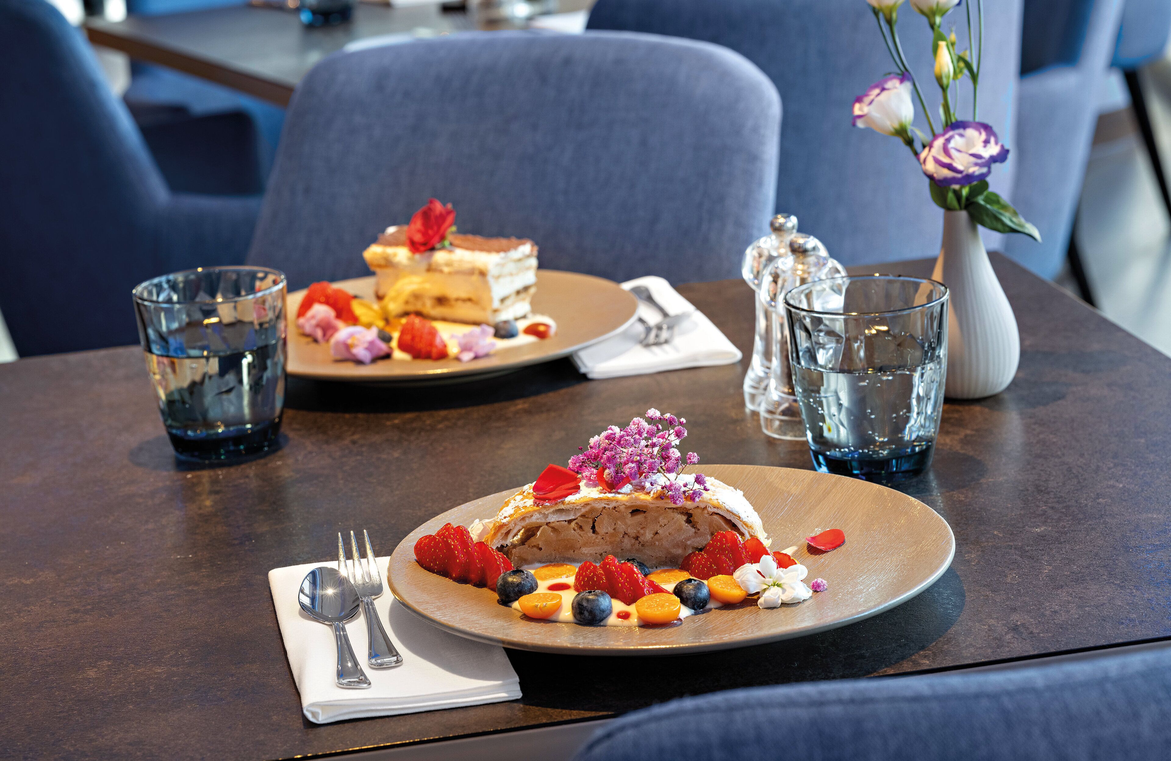 A dining table with a dessert plate, a glass of water, and a vase with flowers.