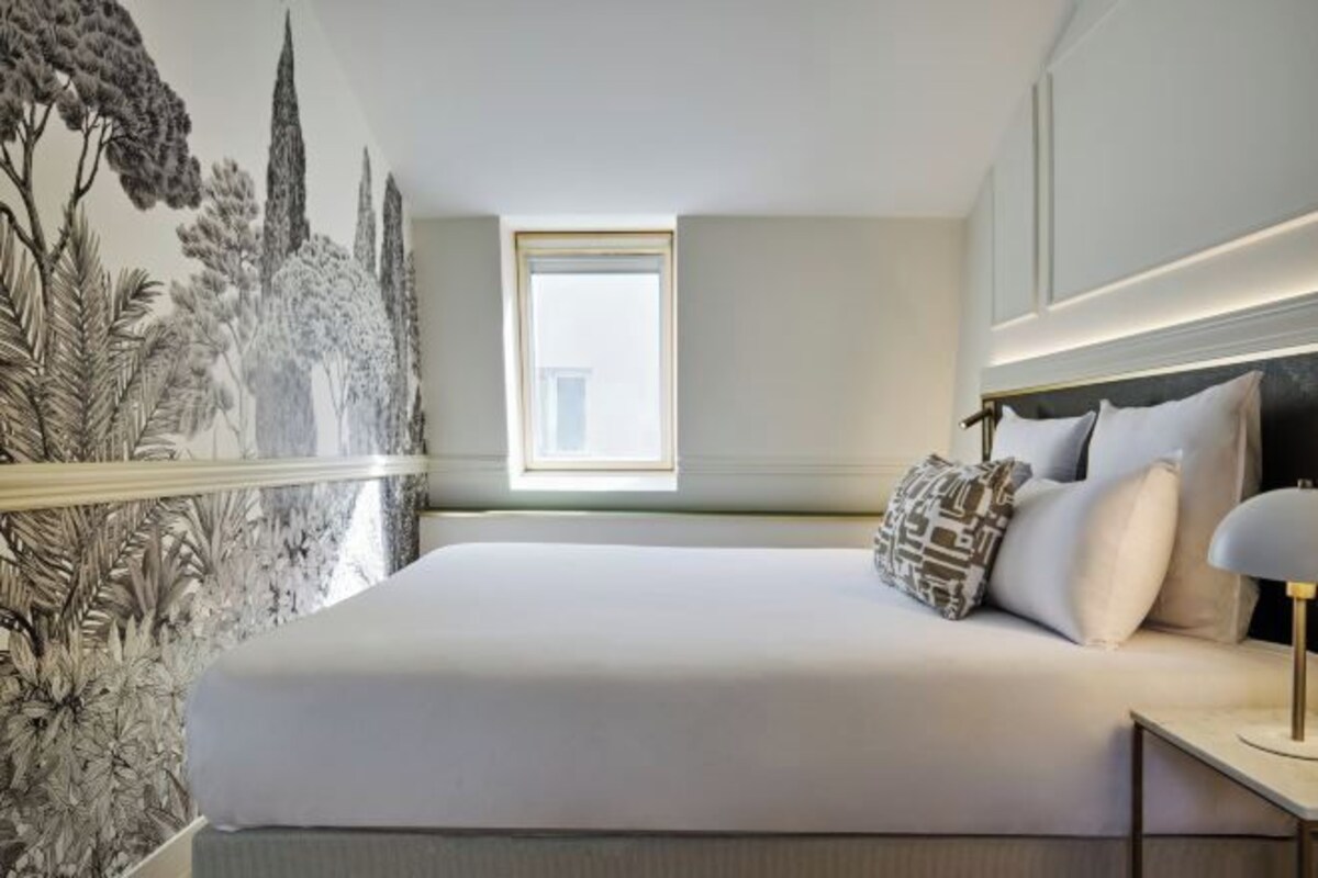 A bedroom with a large bed, a nightstand, a lamp, and a window with a view.