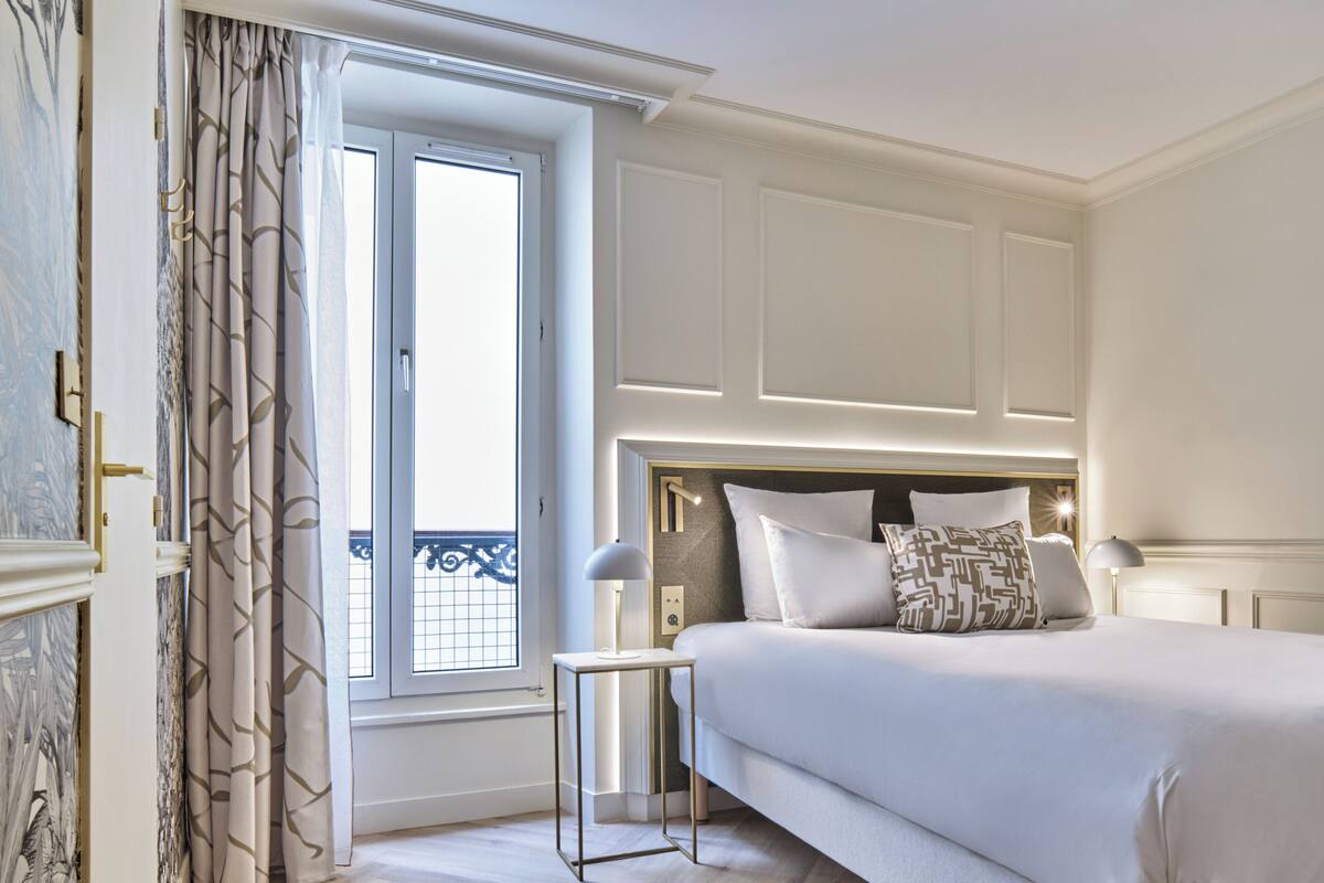 A hotel room with a large bed, a bedside table, and a window with curtains.
