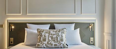 Un lit bien fait, agrémenté d’un coussin à motifs, une tête de lit dotée d’un éclairage intégré et un mur orné de panneaux encastrés.