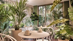 A café with round tables and white chairs, surrounded by various potted plants. - Posy Hotel by Happyculture (Paris)