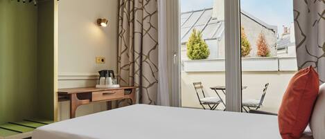Habitación de hotel con cama, escritorio y vista al balcón exterior.