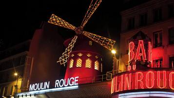 A building with a windmill and illuminated signs reading "MOULIN ROUGE" and "BAR DU MONROU".