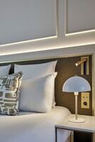 A neatly made bed with white linens and patterned pillows, a bedside lamp, and a wall panel with a textured design.