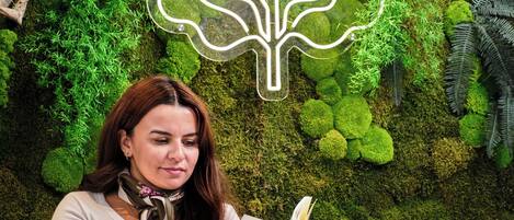 A person sitting at a table with a menu, surrounded by a moss-covered wall with a leaf-shaped light fixture.