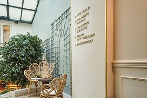 A modern interior with wicker furniture, a glass ceiling, and a wall with directional signs.