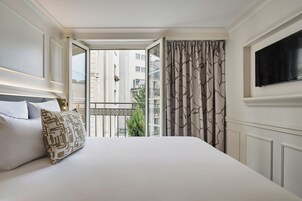 A hotel room with a large bed, a TV mounted on the wall, and a balcony with a view of the city.