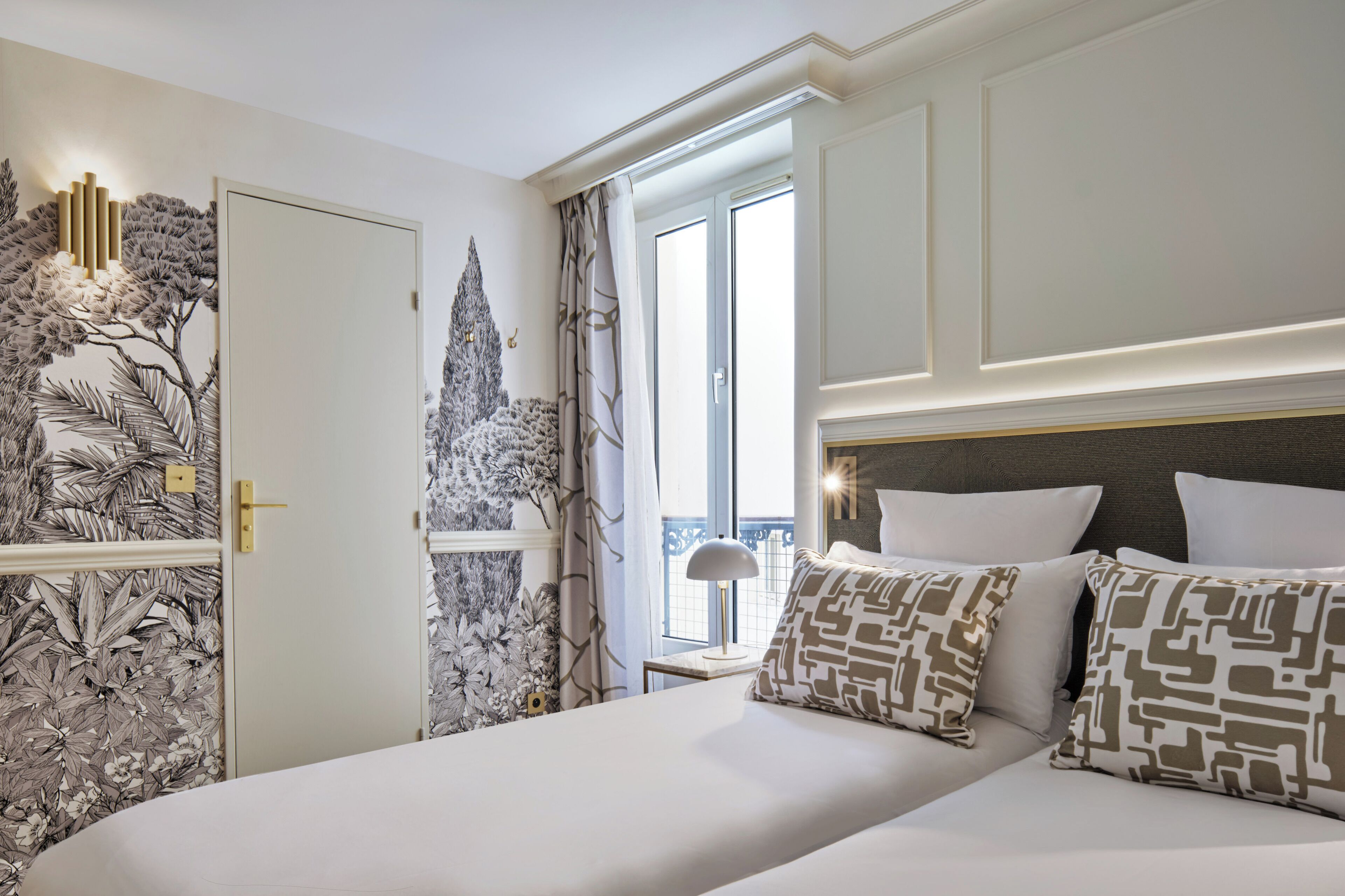Habitación de hotel con una cama grande, una mesita de noche, una lámpara y vistas al exterior.