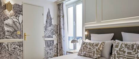 A hotel room with a large bed, a nightstand, a lamp, and a view of the outside.