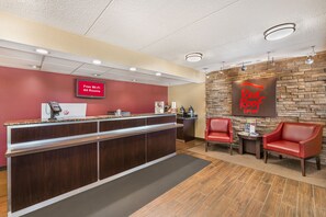 A hotel reception area with a red wall, a 'Free Wi-Fi All Rooms' sign, a 'Red Roof Inn' sign, and two red leather chairs. - Red Roof Inn Erie – I-90 (Erie)