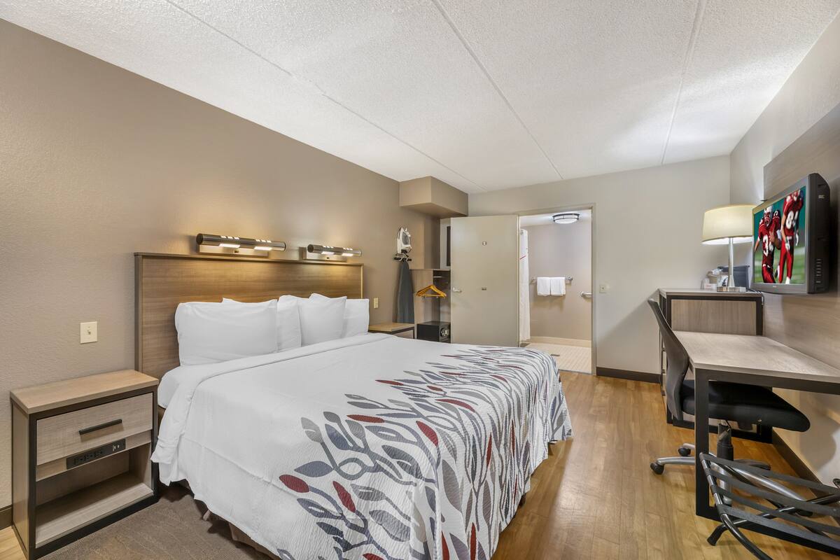 A hotel room with a large bed, a desk, and a chair. There is a door leading to a bathroom and a closet.