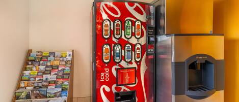 Un distributeur automatique orné du logo Coca-Cola, un point d’eau et un présentoir à magazines contenant divers guides de voyage.