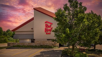 Ett Red Roof Inn-hotell med en fasad av sten, ett rött tak och en parkeringsplats.