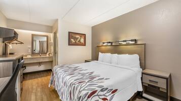 A hotel room with a bed, bedside tables, a desk with a chair, a mirror, and a framed picture on the wall.