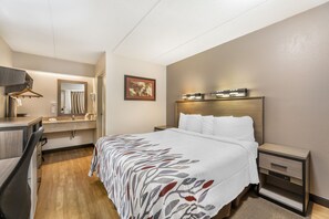 A hotel room with a bed, bedside tables, a desk with a chair, a mirror, and a framed picture on the wall. - Red Roof Inn Erie – I-90 (Erie)