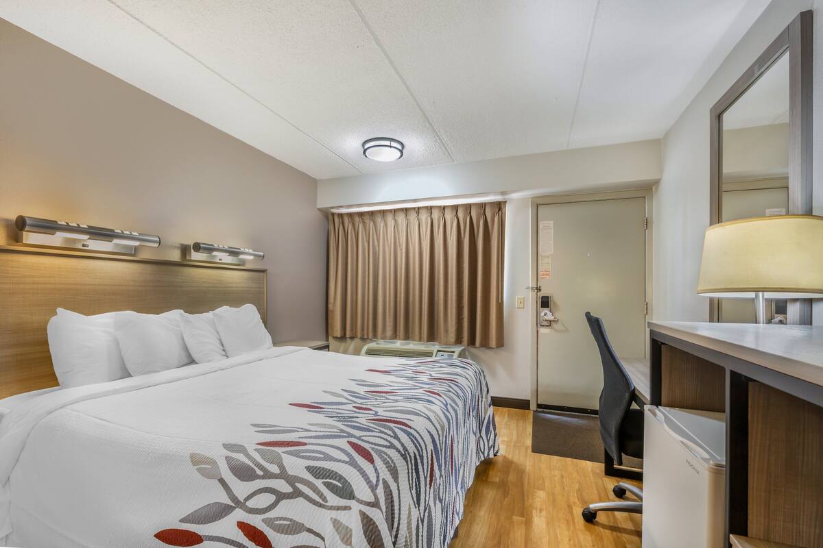 A hotel room with a bed, desk, chair, and a door leading to another room.