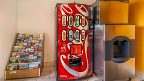 Máquina expendedora con diseño de Coca-Cola, dispensador de hielo y un estante lleno de guías de viaje.