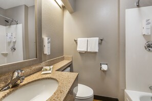 A bathroom with a granite countertop sink, a mirror, a towel rack, a toilet, and a shower area.