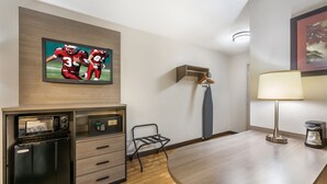 A hotel room with a flat-screen TV mounted on the wall, a minibar, a desk with a lamp, and a chair. - Red Roof Inn Erie – I-90 (Erie)