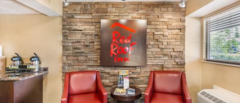 Vestíbulo de Red Roof Inn con pared de piedra, dos sillones de cuero rojo, una mesita con comodidades y vistas a través de la ventana.