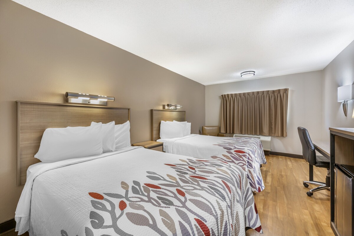Una camera d'albergo con due letti, una scrivania e una sedia.