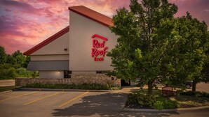 Un hotel Red Roof Inn con fachada de piedra, un estacionamiento y un camino de entrada bordeado de árboles.