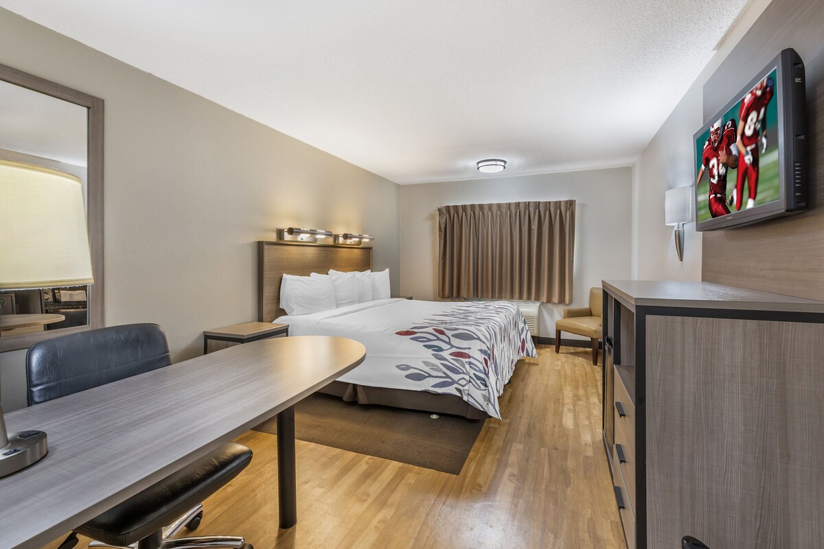 Una camera d'albergo con un letto, una scrivania, una sedia, una televisione e un armadio.