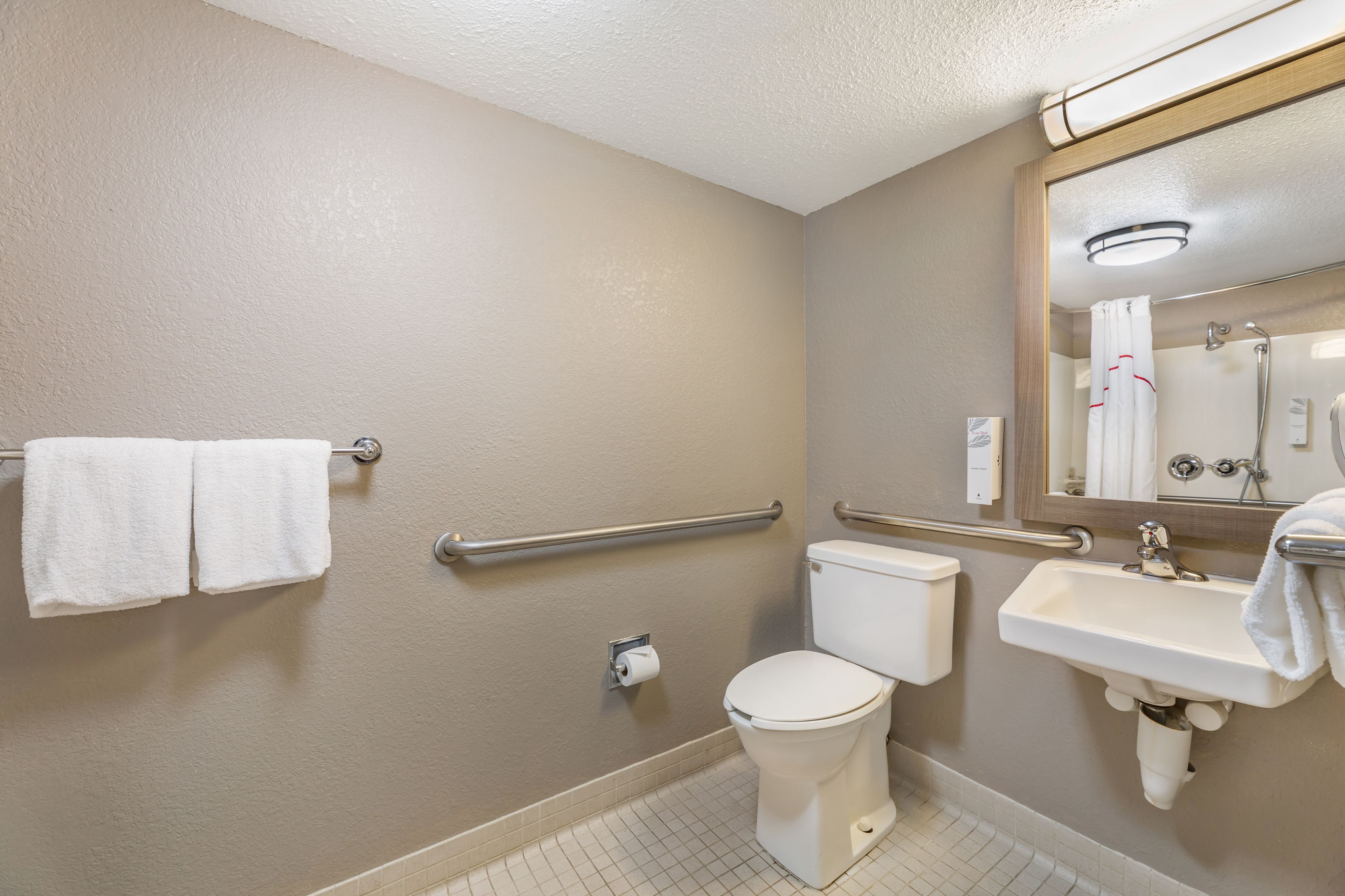 A standard hotel bathroom with a toilet, sink, and hand soap dispenser.