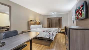 A hotel room with a bed, a desk, a chair, a TV, and a window with curtains.