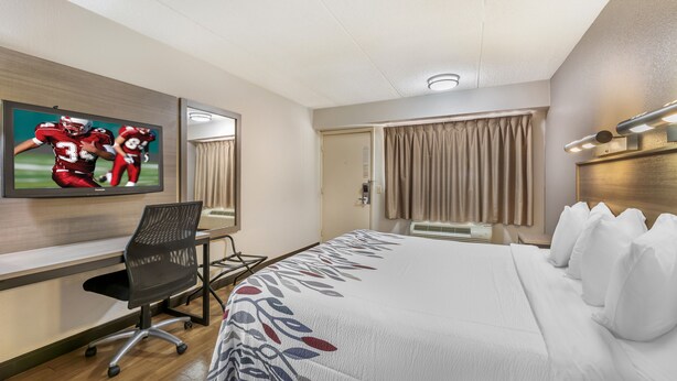 A hotel room with a bed, a desk, a chair, a television, and a window with curtains. - Red Roof Inn Erie – I-90 (Erie)