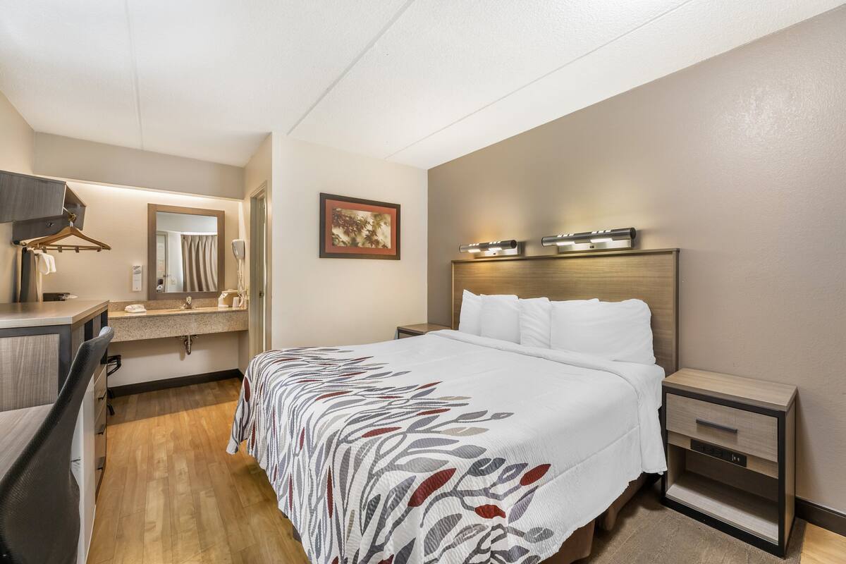 A hotel room with a bed, bedside tables, a desk, a chair, a mirror, and a framed picture on the wall.