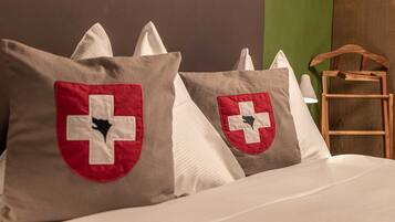 A bed with pillows featuring a red and white cross design, a wooden chair, and a green wall in the background.
