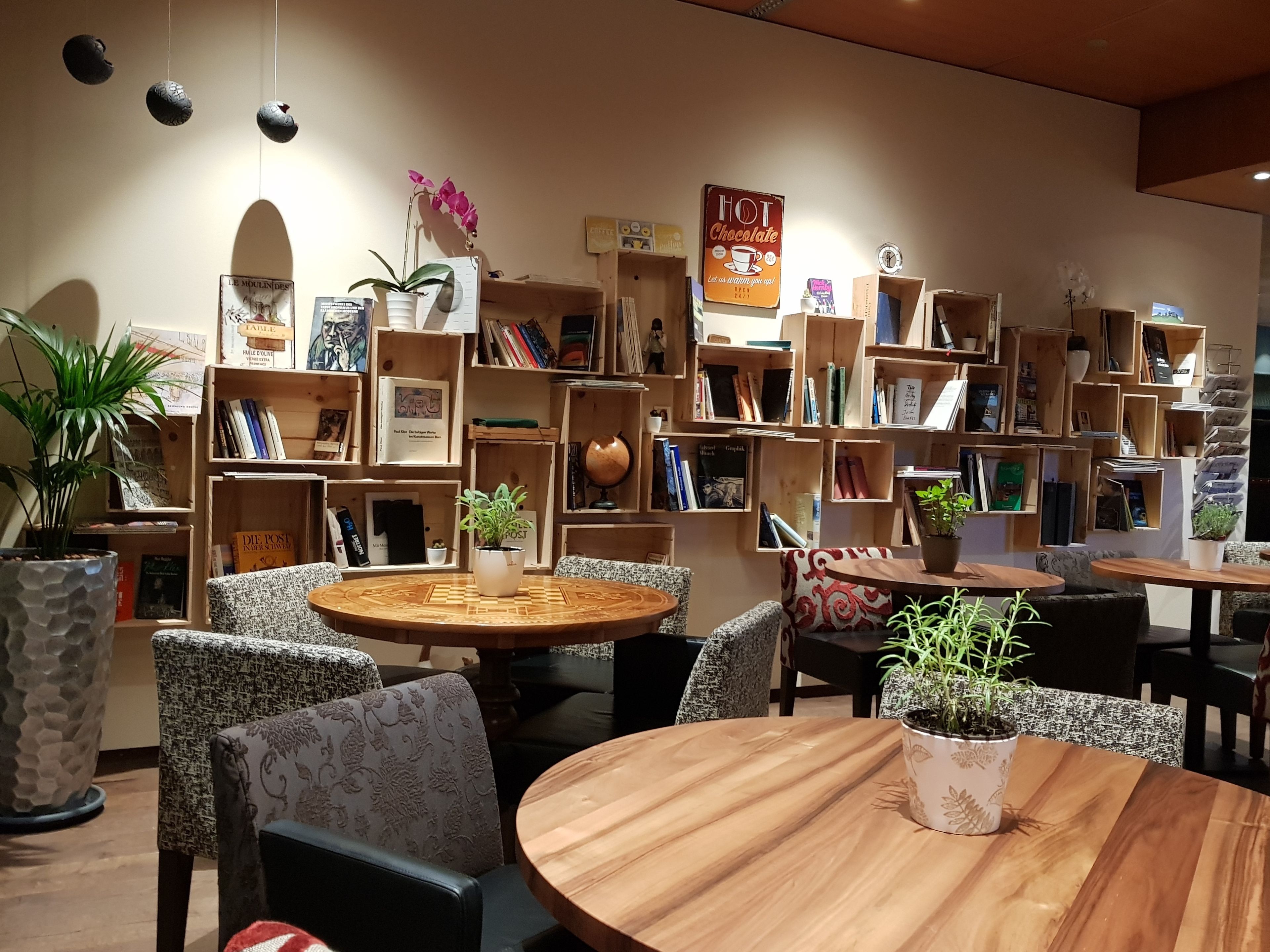 Un coin lecture accueillant, avec une table ronde en bois, des fauteuils confortables et différentes étagères remplies de livres et d’objets décoratifs.