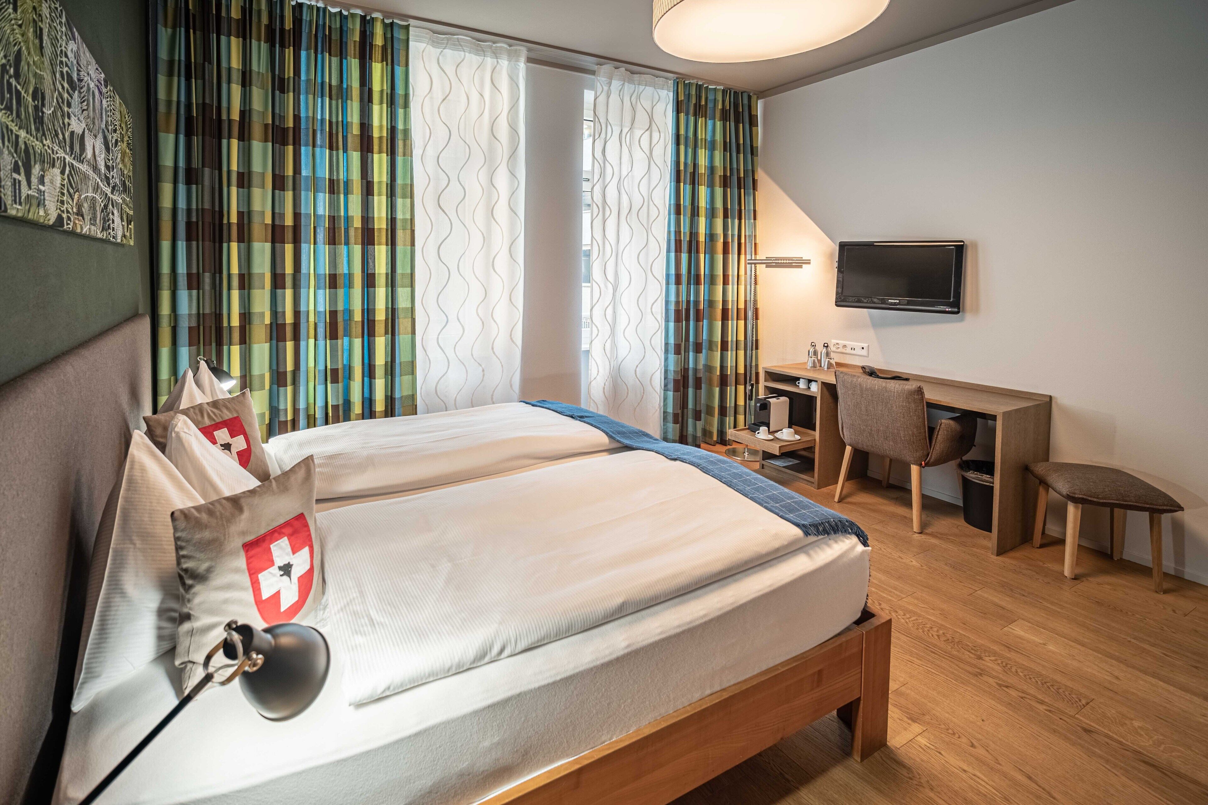 Een hotelkamer met een bed, een bureau, een stoel, een televisie en gordijnen.