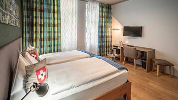 Een hotelkamer met een bed, een bureau, een stoel, een televisie en gordijnen.