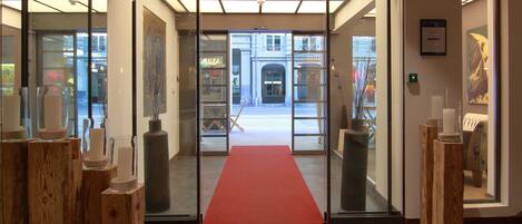A hotel entrance with a red carpet, wooden pillars, and a view of the street outside.