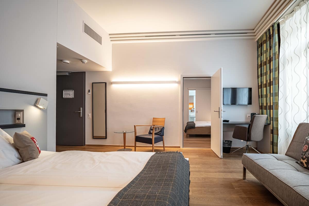 A hotel room with a bed, a sofa, a desk, and a chair.