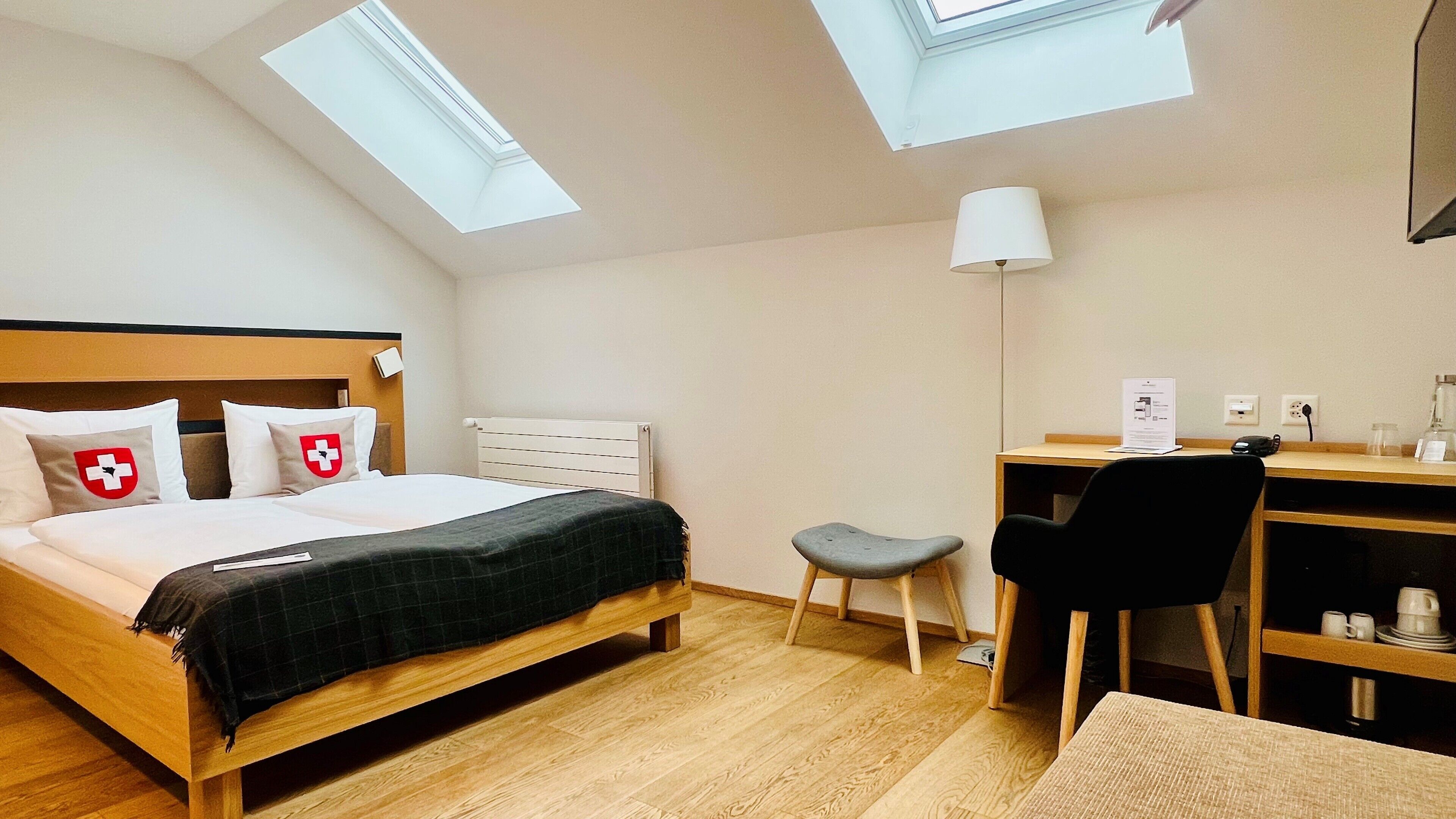 A hotel room with a bed, desk, chair, and skylights.